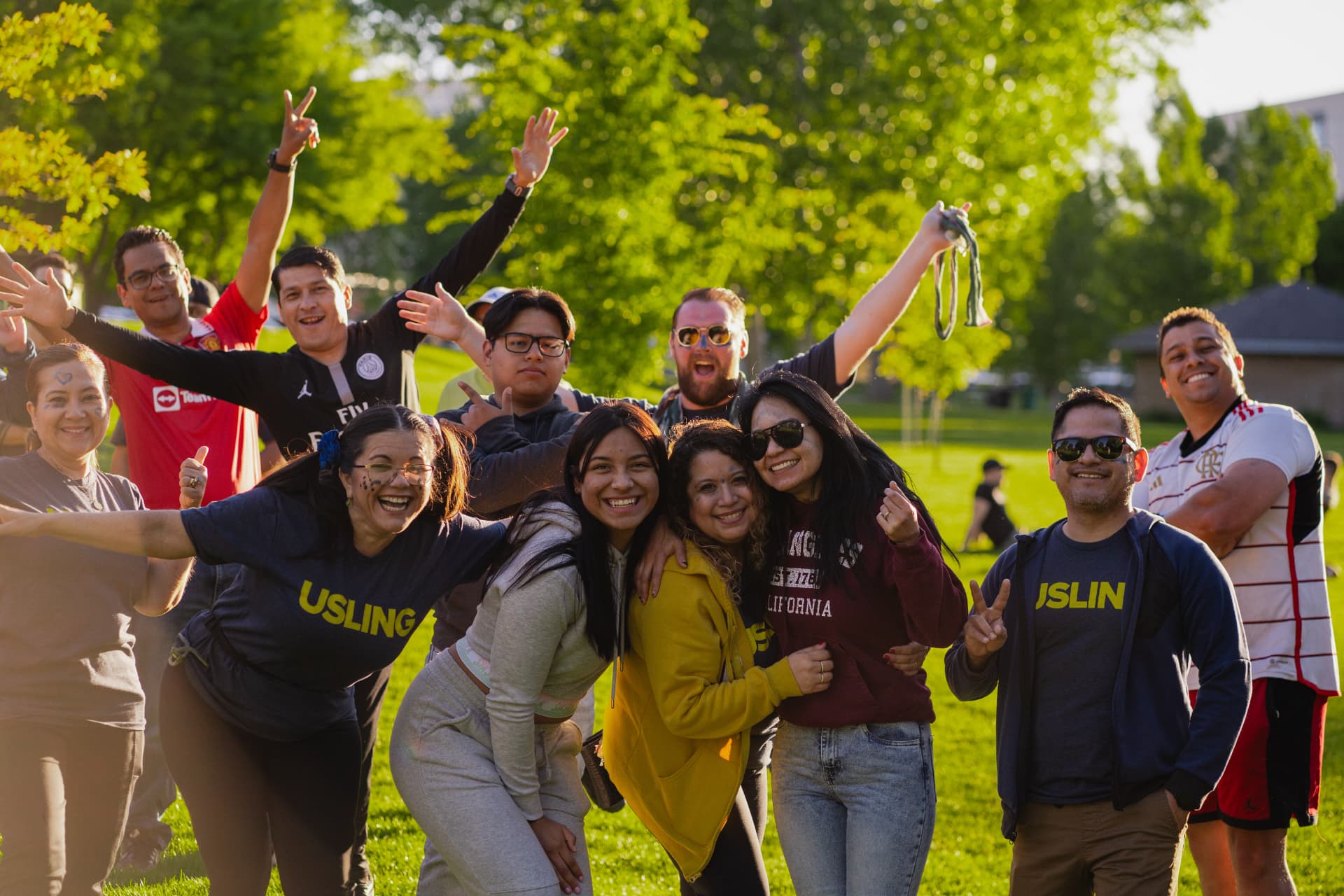 USLING students and staff gathered outdoors on a grassy hill, smiling and waving